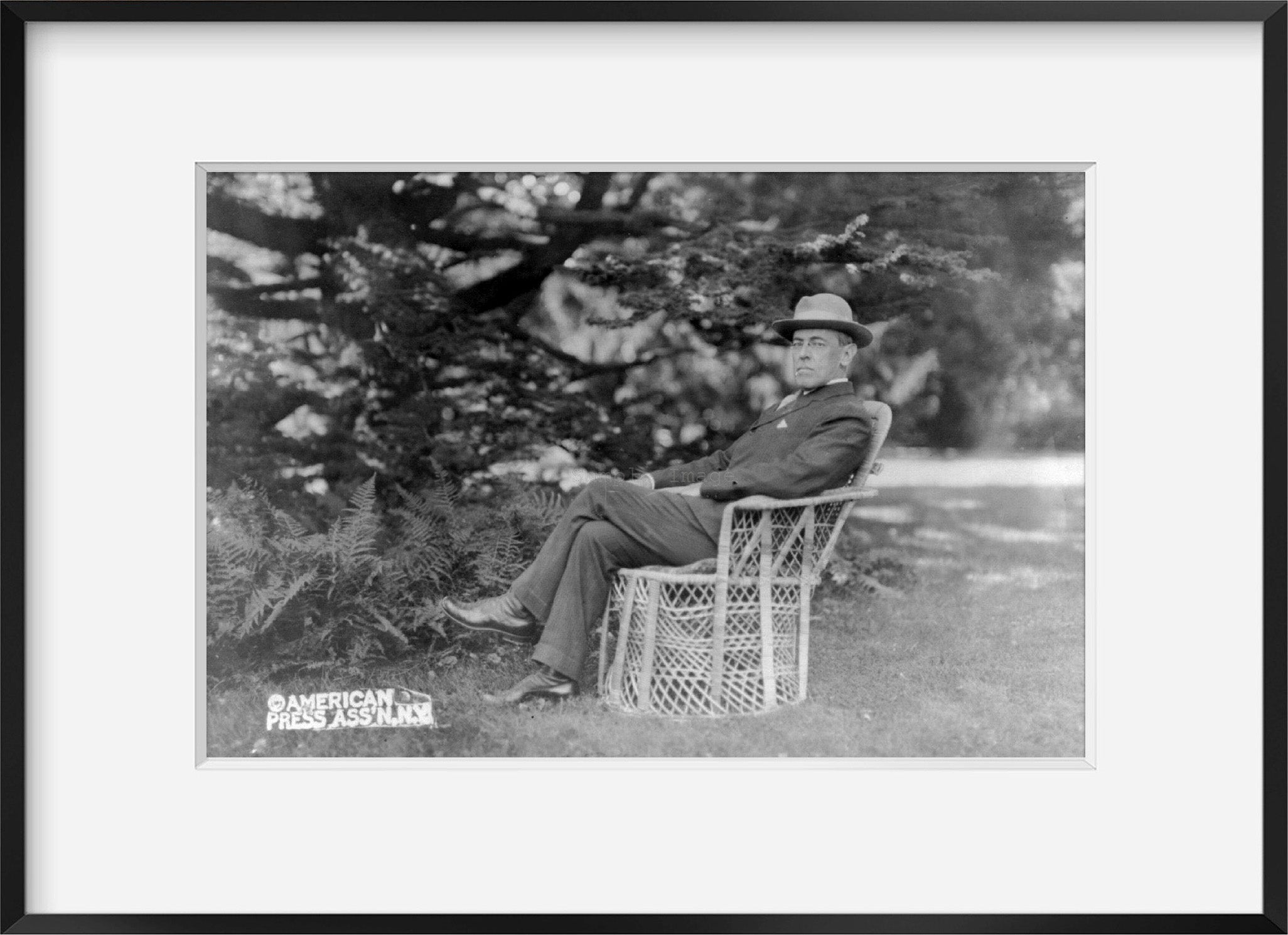 c1910 photograph of Woodrow Wilson, full, seated in wicker chair on lawn of Pros
